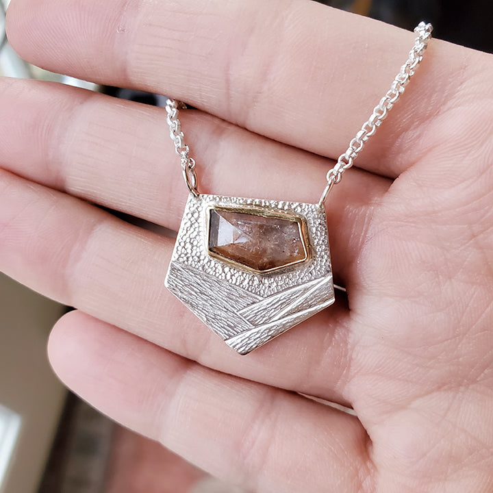 orange specked faceted gemstone set in yellow gold on textured silver plate