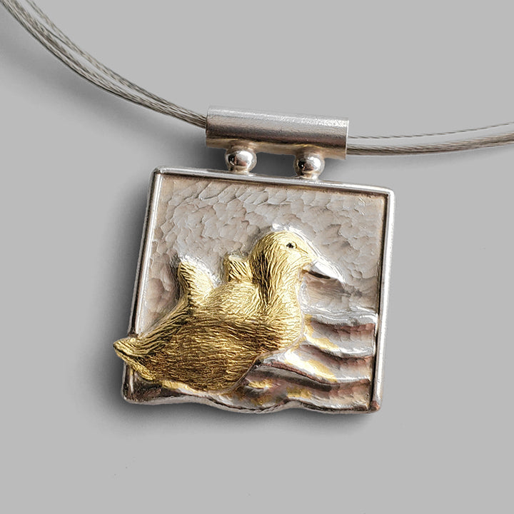 square silver pendant with baby bird in gold in water