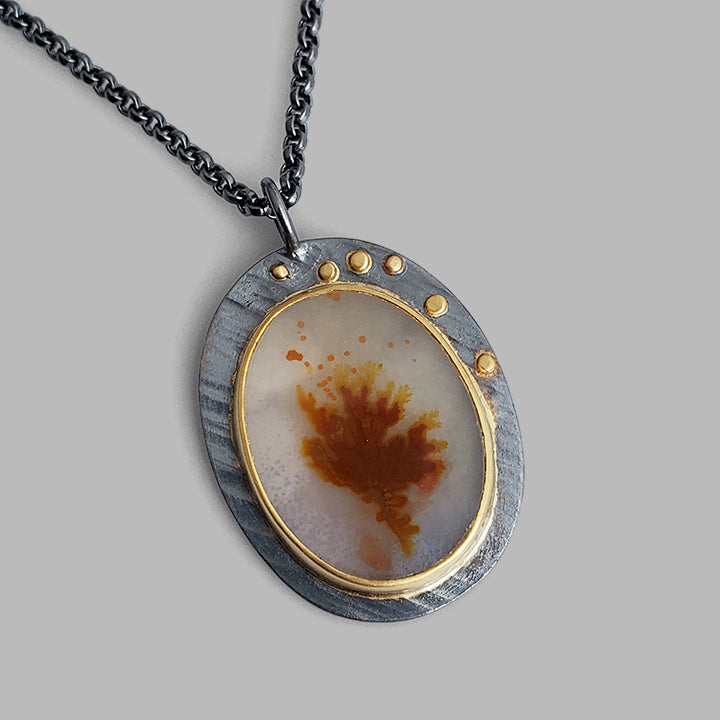 orange and white plant life gemstone set in gold on oxidized oval plate on chain