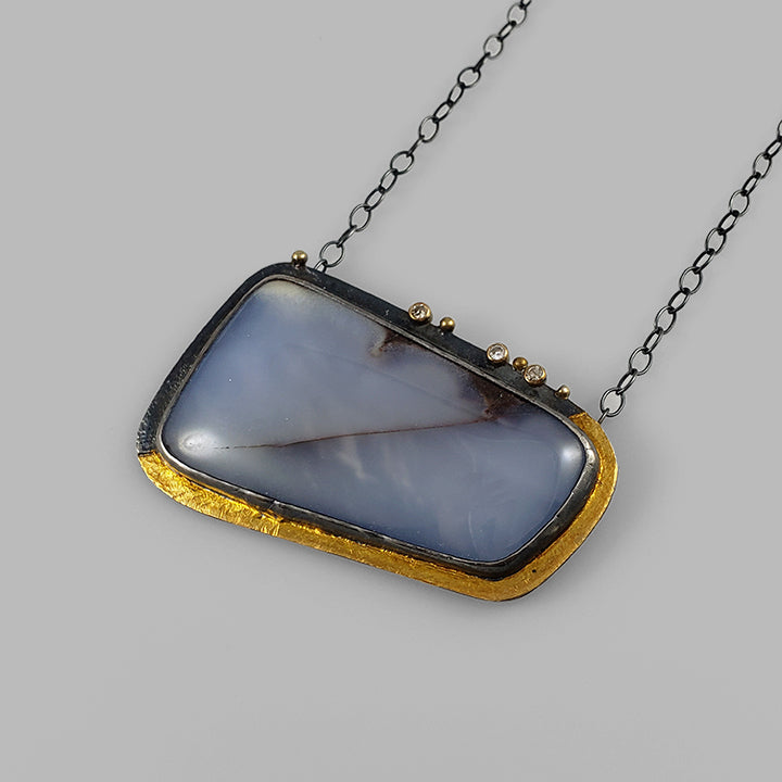 large periwinkle gemstone set in oxidized silver on textured plate in silver and gold with diamonds