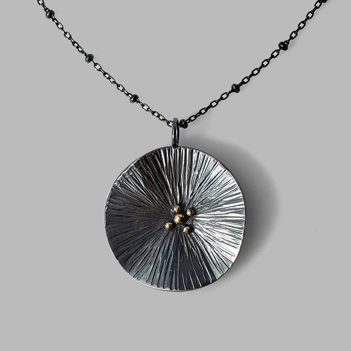 round textured organic oxidized silver pendant with gold dots on chain