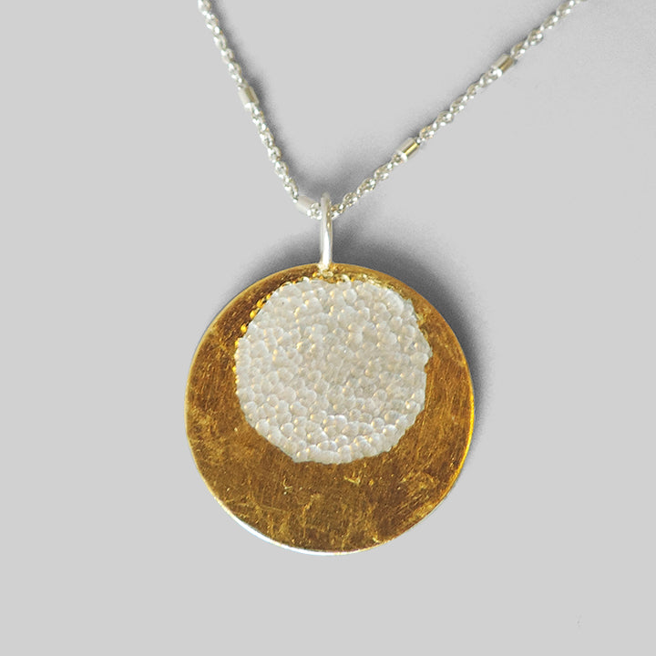 round silver pendant with gold layered around hammered circle on long chain