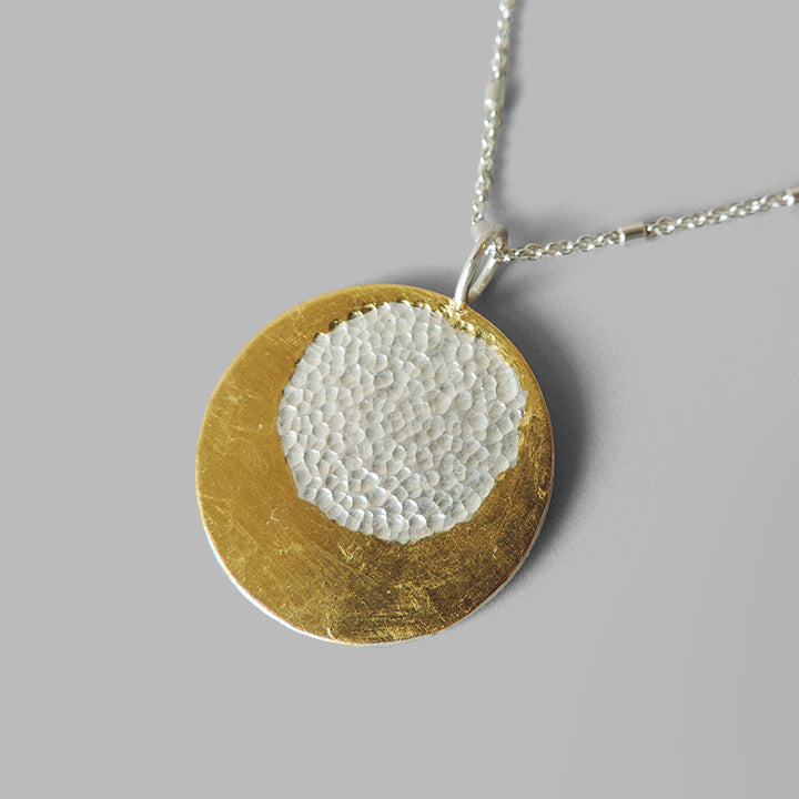 round silver pendant with gold layered around hammered circle on long chain