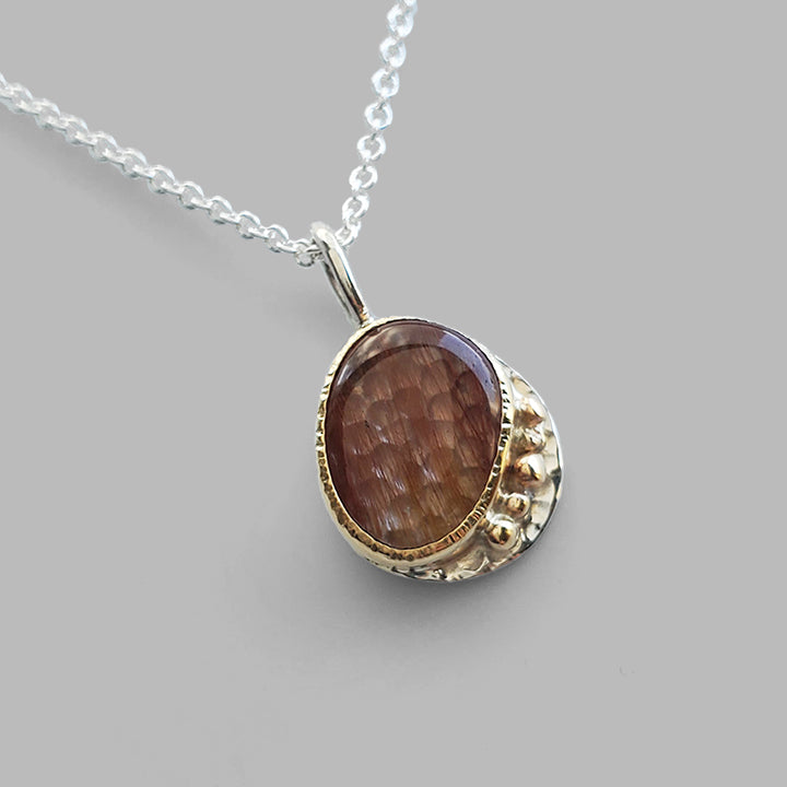 red striped clear gemstone set in yellow gold bezel on textured silver plate with gold dots