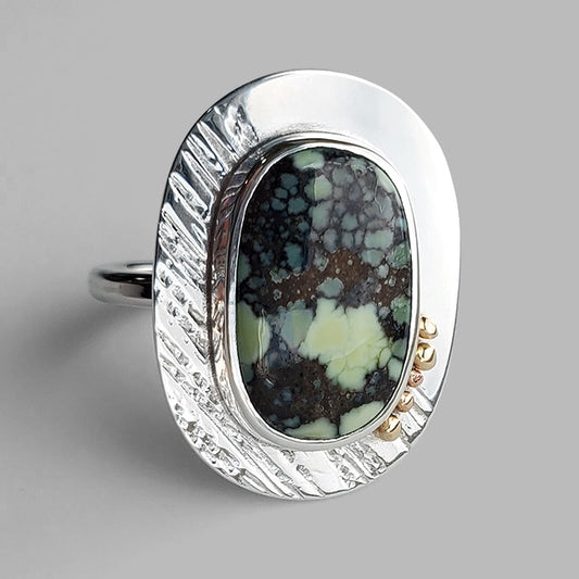 light green and black stone on textured silver plate with gold dots